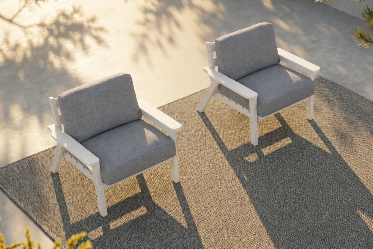 Two outdoor armchairs with creamy white frames and gray cushions, arranged on a textured gray rug in a sunlit patio setting.