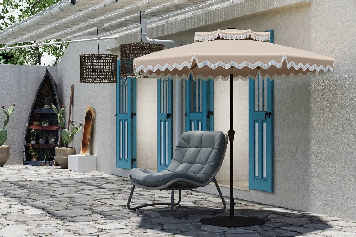 Beige patio umbrella with decorative trim over a gray chair on a stone patio.