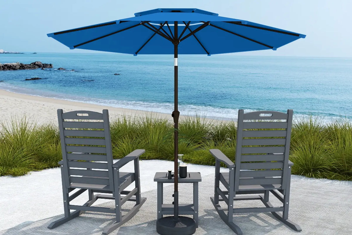 Two gray chairs with a blue umbrella on a sandy beach.