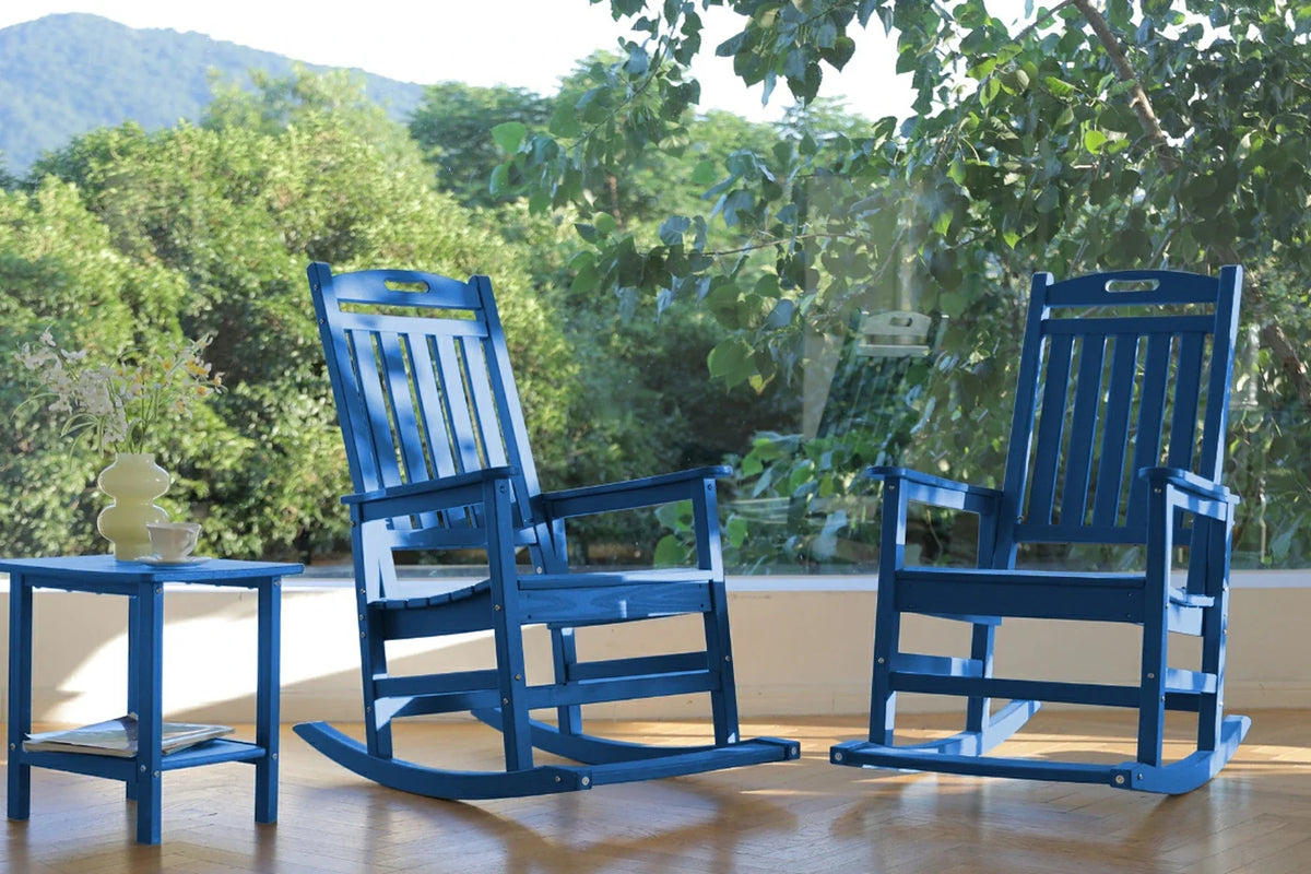 Two blue rocking chairs on a wooden floor with a scenic background of trees and mountains.