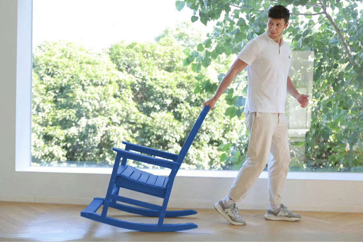 Person pushing a blue rocking chair indoors with a large window showing greenery outside.