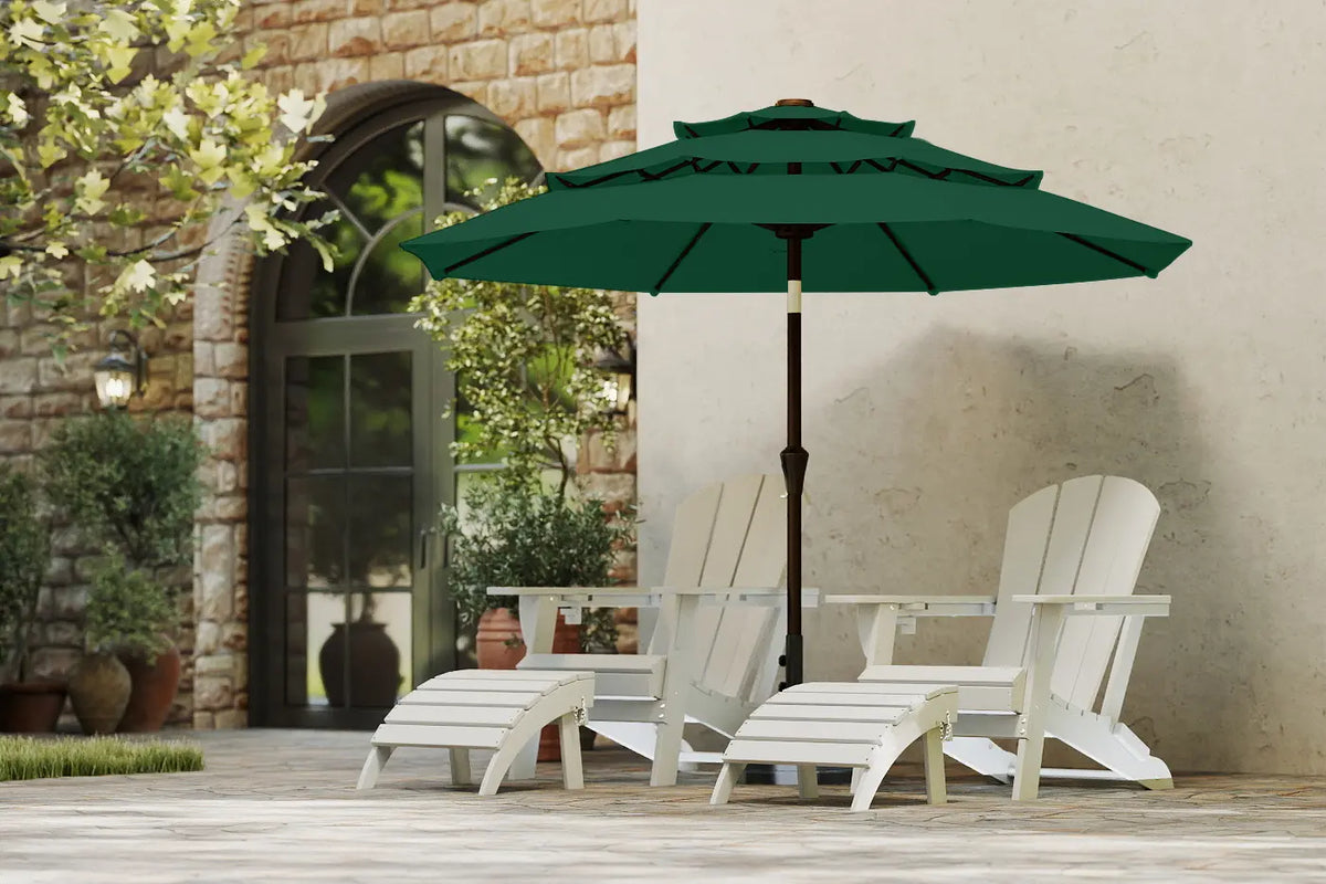Green patio umbrella over white Adirondack chairs on a patio with stone wall and door in the background.