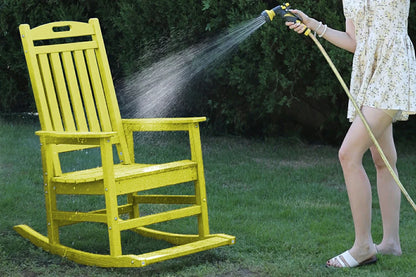 Person cleaning a yellow rocking chair with a hose on a grassy area.