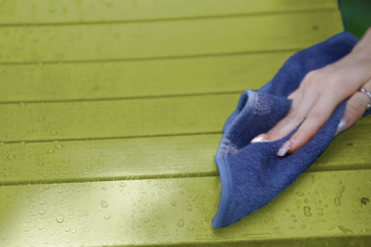 Hand using a blue cloth to wipe a green wooden surface