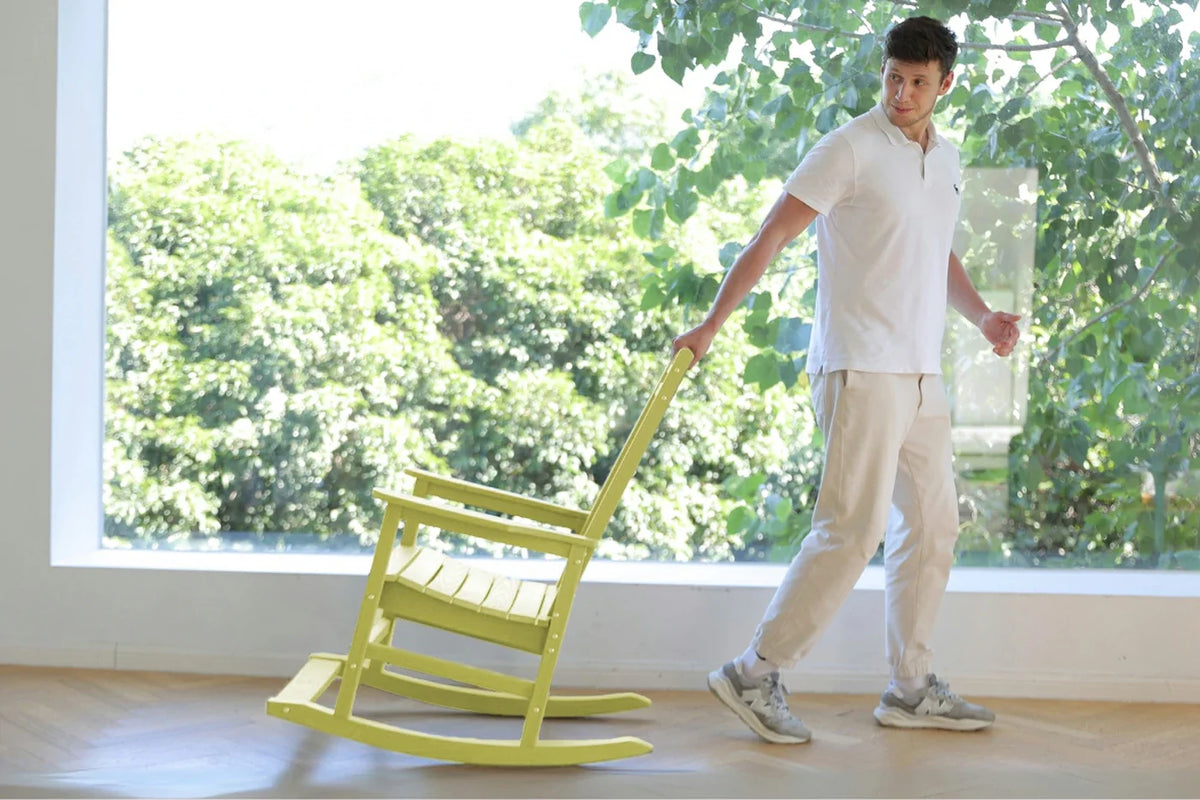 Person pushing a green rocking chair indoors with a large window showing greenery outside.