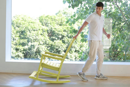 Person pushing a green rocking chair indoors with a large window showing greenery outside.