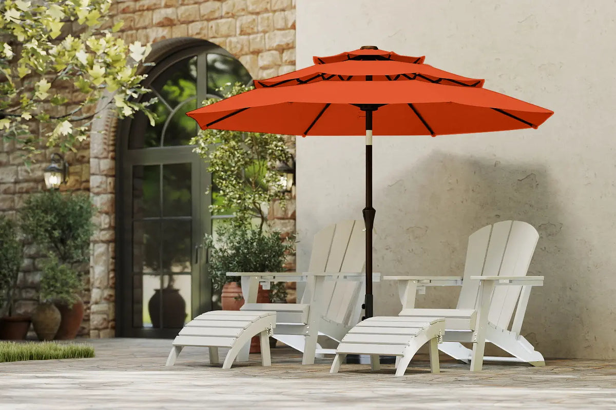 Orange patio umbrella over white chairs on a wooden deck with a stone wall background