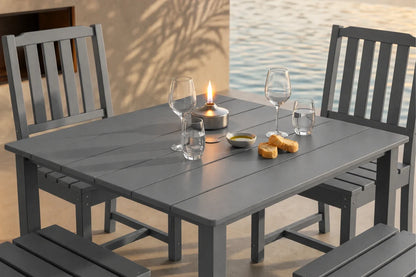 Gray outdoor dining table with 4 armless chairs and glasses by a body of water.