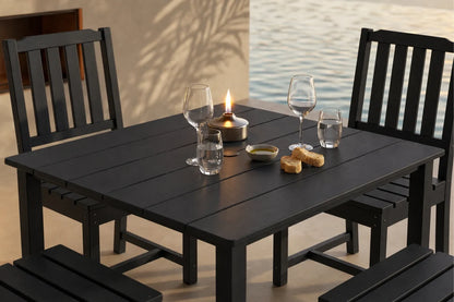 Black outdoor table with 4 armless chairs and glasses by a body of water