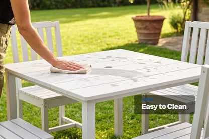 Person cleaning a white outdoor table with 4 armless chairs in a garden setting, emphasizing ease of cleaning.