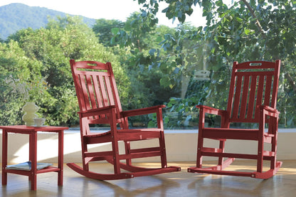 Two red rocking chairs on a wooden floor with a scenic background of trees.