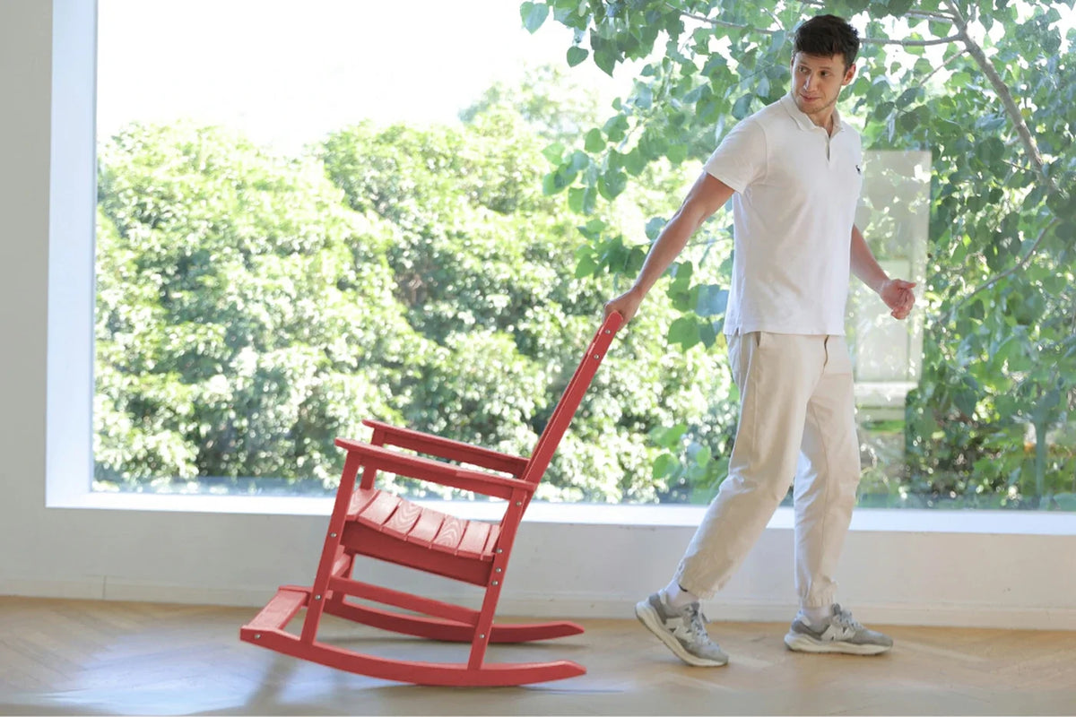 Person pushing a red rocking chair indoors with a large window showing greenery outside.