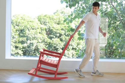 Person pushing a red rocking chair indoors with a large window showing greenery outside.
