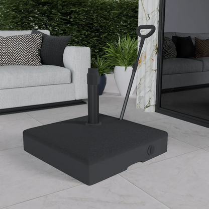 A black outdoor umbrella base with a handle, placed on a tiled floor, with a sofa and cushions in the background.