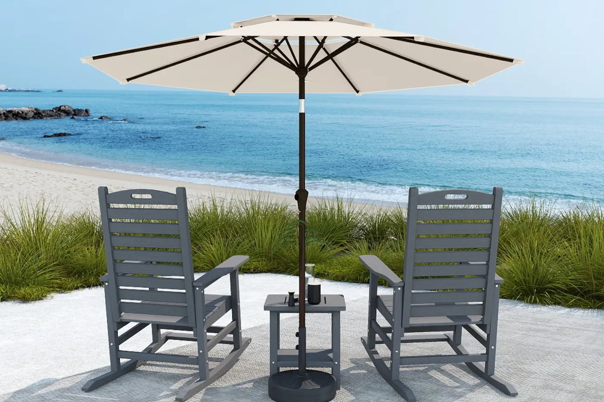 Two gray chairs with a matching table and umbrella on a sandy beach.