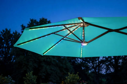 An aruba blue patio umbrella with integrated RGB LED lighting glowing along the ribs and canopy, shown against a dark blue twilight sky and silhouetted trees.
