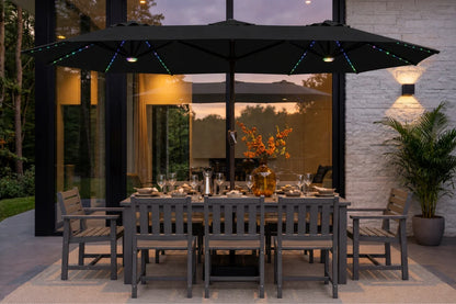 A large black patio umbrella with integrated RGB LED string lights is shown over a dining table and chairs on a patio outside a modern house at dusk.