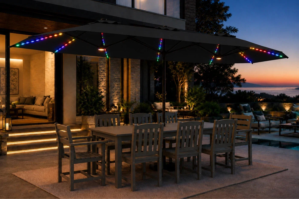A large black patio umbrella with multicolor RGB LED string lights along the canopy edges, shading an outdoor dining table and chairs on a patio at dusk.