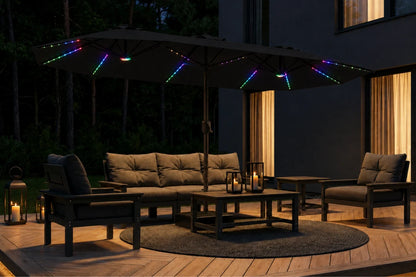 Outdoor patio furniture set under a large patio umbrella with multicolor RGB LED string lights, including a sectional sofa, two armchairs, a coffee table, and lanterns on a wooden deck at night.