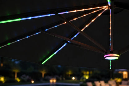 Black outdoor RGB LED umbrella string lights glowing in multiple colors along the ribs of a dark patio umbrella at night.