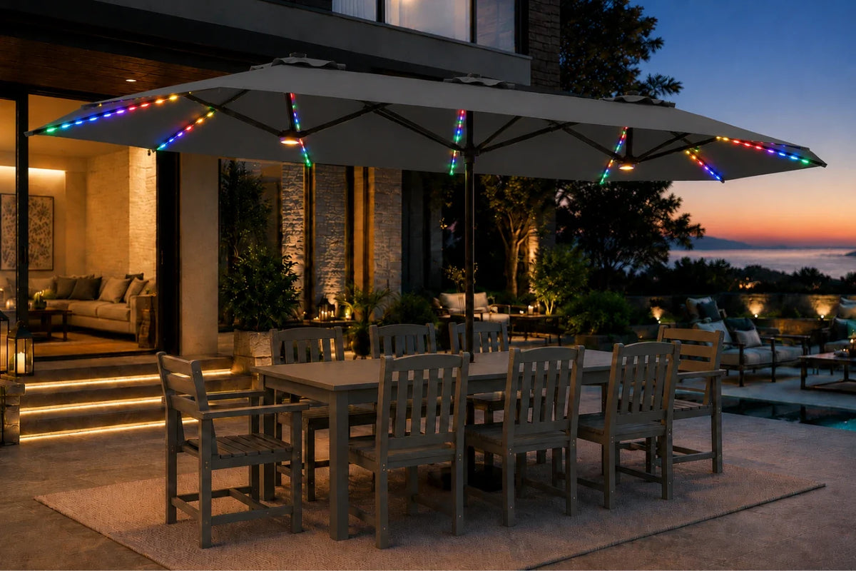 A large dark gray outdoor patio umbrella with a matching dining table and chairs on a patio at dusk, decorated with multicolor RGB LED string lights along the canopy and frame.
