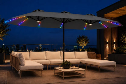 Outdoor patio furniture set with a large sectional sofa, matching ottoman, and coffee table under a dark gray patio umbrella with colorful RGB LED string lights at night.
