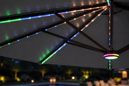 Multicolor RGB LED string lights glowing along the metal frame of a dark gray patio umbrella at night, with a blurred outdoor background.