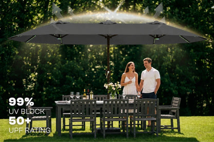 A large dark gray outdoor patio umbrella shown in a backyard setting with a couple standing underneath. Text on the left reads '99% UV BLOCK 50+ UPF RATING'.