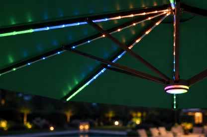 Multicolor RGB LED string lights running along the metal frame of a dark green patio umbrella at night, with a poolside background.
