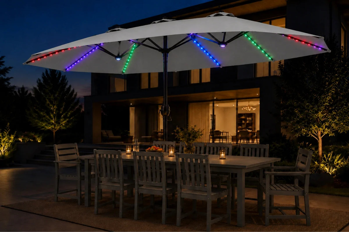 A large gray outdoor patio umbrella with integrated RGB LED string lights glowing in blue, green, red, and purple, shading a dining table and chairs on a patio at dusk in front of a modern house.