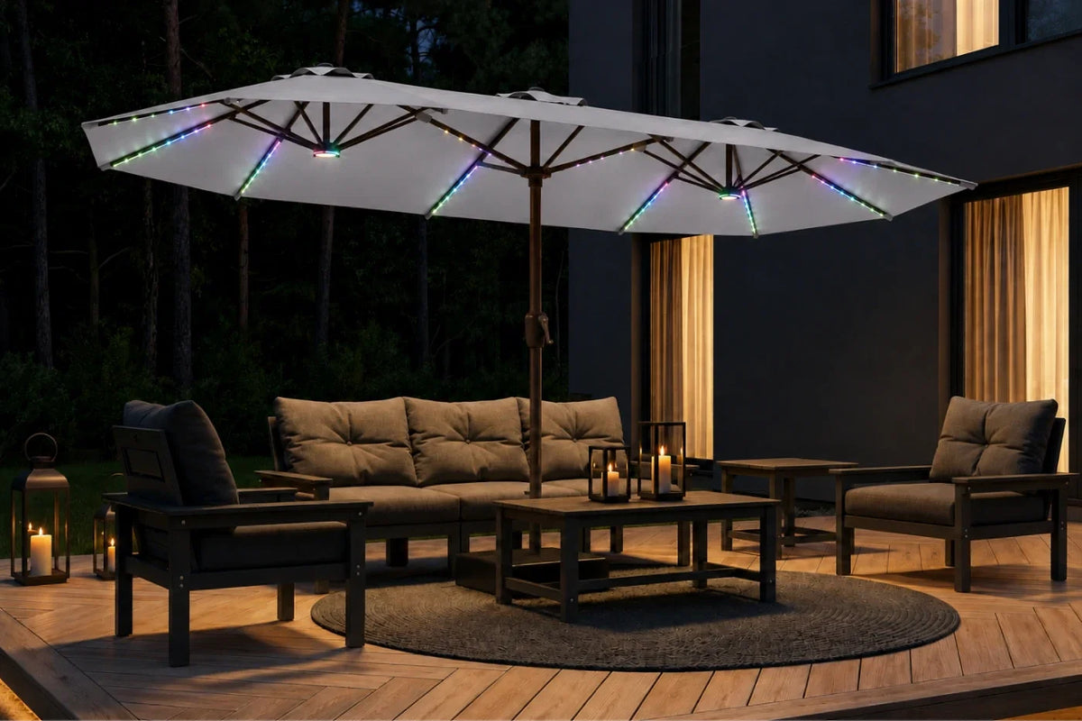 A large gray patio umbrella with integrated multicolor RGB LED string lights stands over a modern outdoor patio furniture set including a sofa, two armchairs, and a coffee table on a wooden deck at night.