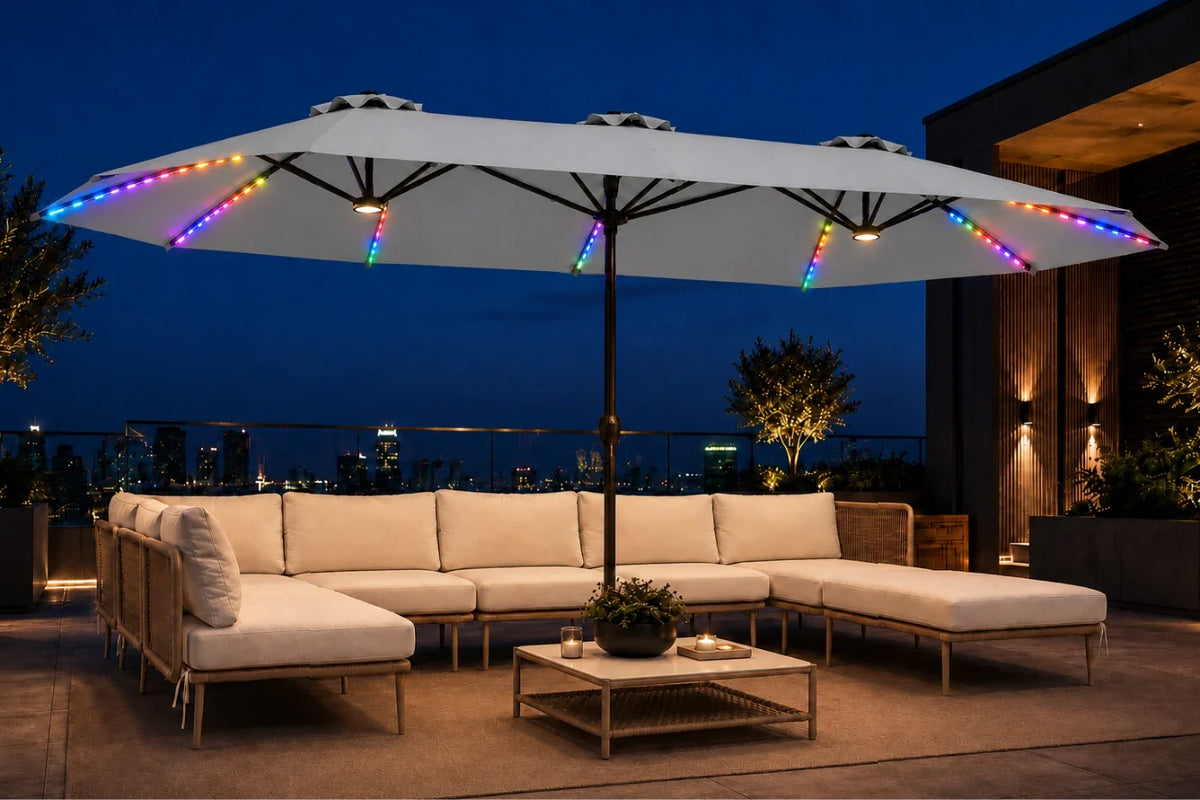 A large gray patio umbrella with colorful RGB LED string lights along the canopy edges, shading a beige outdoor sectional sofa and coffee table on a rooftop terrace at dusk.