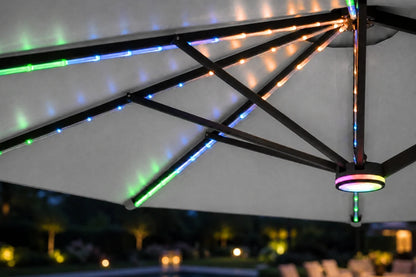 Multicolor RGB LED string lights running along the underside of a gray patio umbrella, with a circular RGB light fixture at the center, shown in an outdoor nighttime setting.