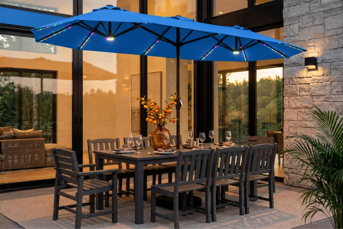 A indigo blue patio umbrella with integrated RGB LED lighting is shown outdoors over a dark gray dining table and chairs on a patio in front of a modern glass house.
