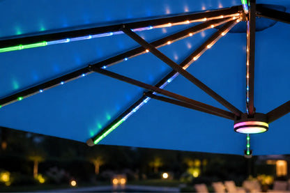 Multicolor RGB LED strip lights running along the underside of a large patio umbrella, casting blue, green, and orange glow against a dark blue evening sky.