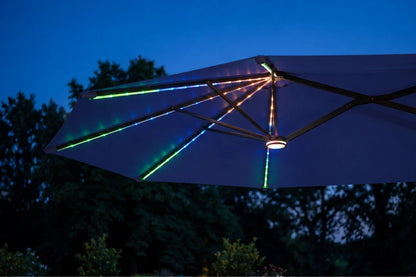 A large navy blue patio umbrella at dusk with RGB LED lighting strips glowing along the ribs and canopy, set against a dark blue evening sky and silhouetted trees.