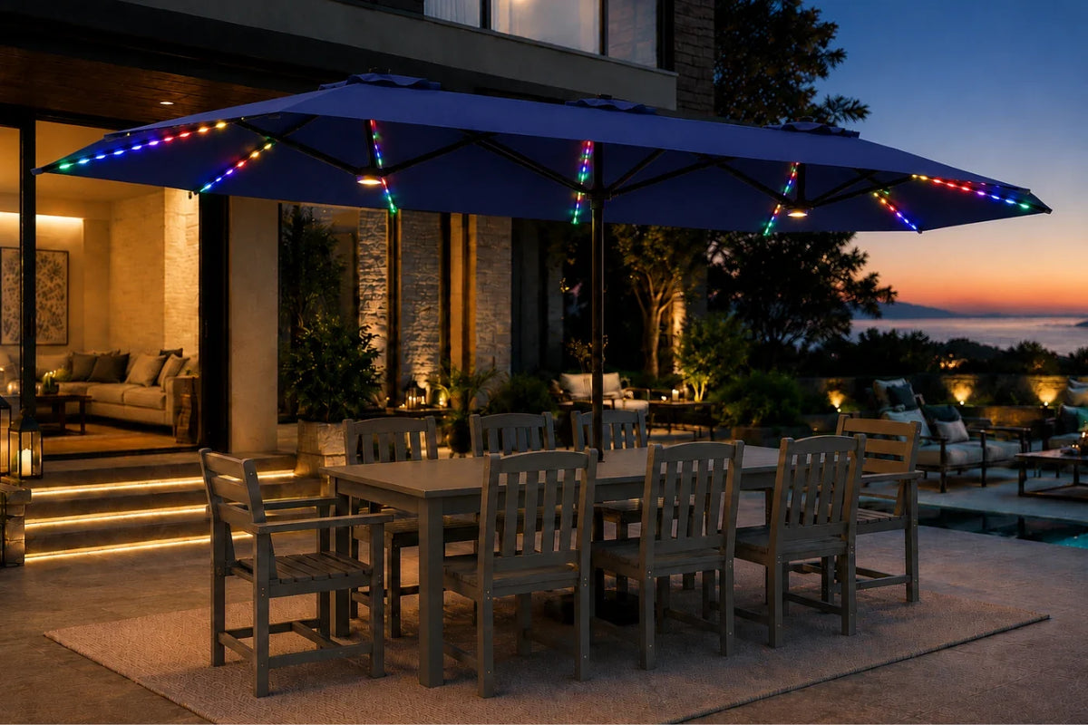 A large navy blue patio umbrella with multicolor RGB LED string lights draped along the canopy and frame, set over an outdoor dining table and chairs on a patio at dusk.