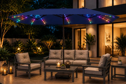 A large navy blue outdoor patio umbrella with colorful RGB LED string lights draped over it, shading a modern patio furniture set with gray cushions and a coffee table at night.