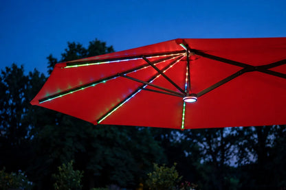 A red patio umbrella with integrated RGB LED lighting glowing along the ribs, photographed outdoors against a dark blue evening sky and silhouetted trees.