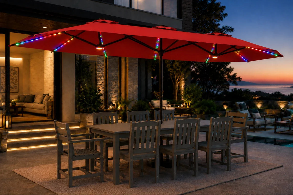A large red outdoor patio umbrella with multicolor string lights draped along the canopy and frame, shading a dining table and chairs on a patio at dusk.
