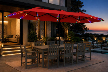 A large red outdoor patio umbrella with multicolor string lights draped along the canopy and frame, shading a dining table and chairs on a patio at dusk.
