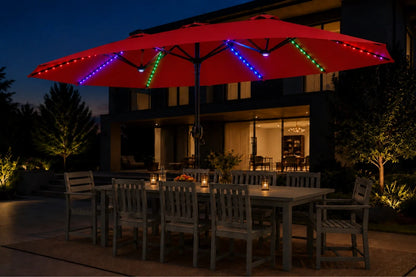 A large red patio umbrella with colorful RGB LED string lights, and red, set up on an outdoor dining patio at night in front of a modern house.