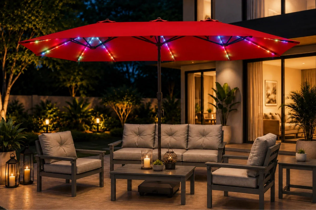 A large red outdoor patio umbrella with colorful string lights draped over it, shading a modern patio furniture set including a sofa, two armchairs, and a coffee table at night.
