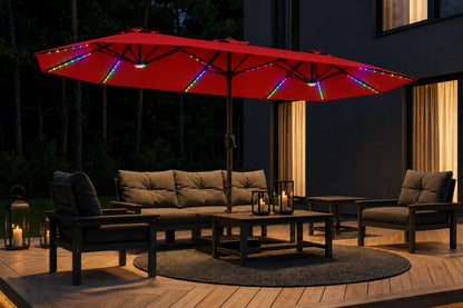 A large red patio umbrella with multicolor RGB LED string lights draped along the edges, shading an outdoor patio furniture set including a sofa, two armchairs, and a coffee table on a wooden deck at night.