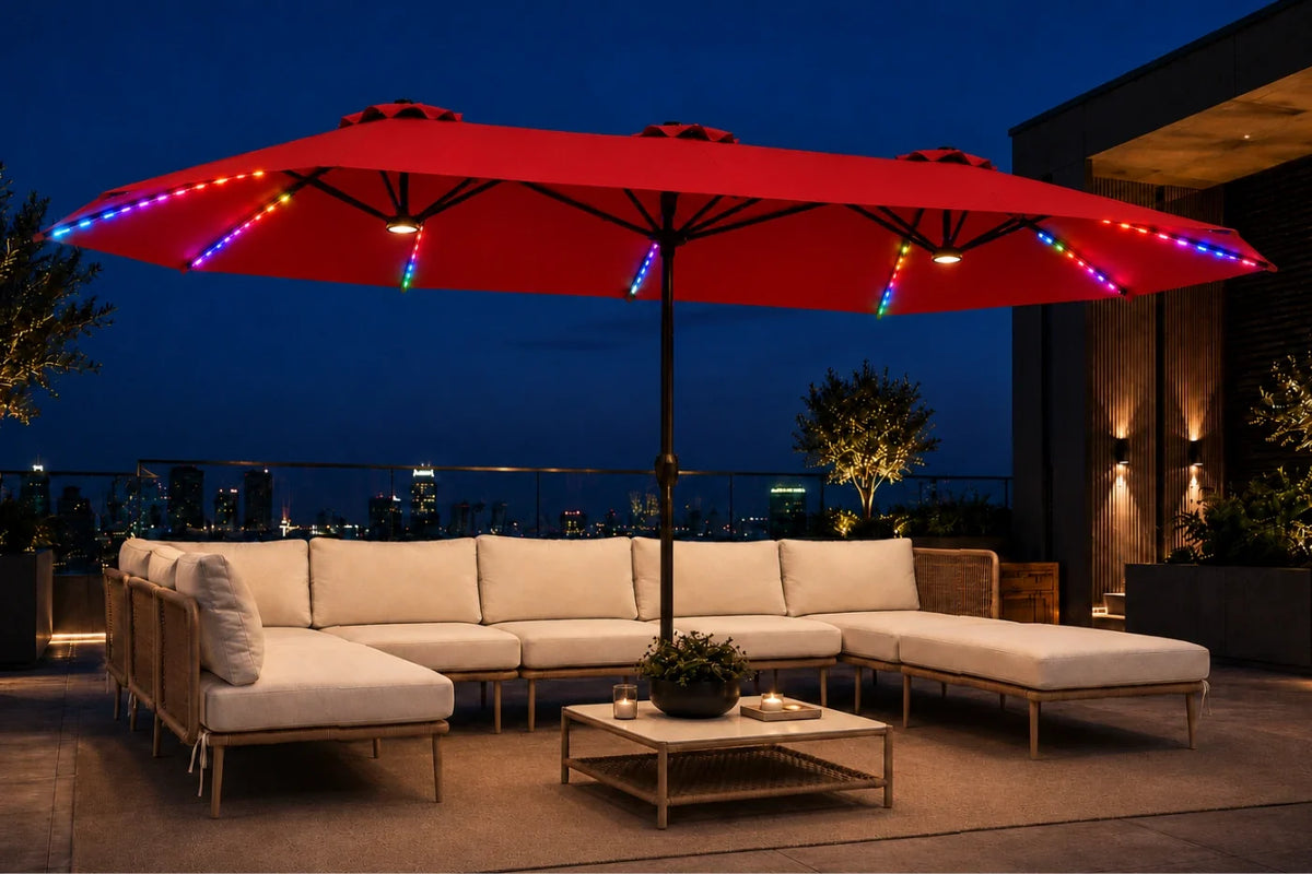A large red patio umbrella with colorful RGB LED string lights is shown on a rooftop terrace at night, shading a cream sectional sofa and a small coffee table.