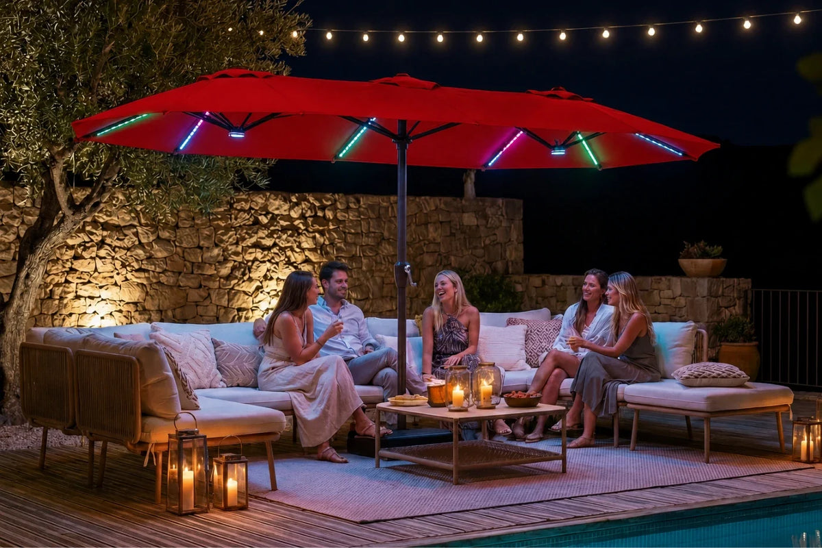 Outdoor patio scene at night with a large red patio umbrella featuring colorful RGB LED light strips, shading a group of four people sitting on a beige sectional sofa. A stone wall, string lights, candles, and a pool are visible in the background.