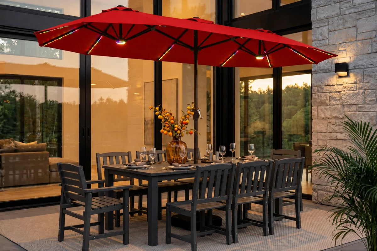 A red patio umbrella with integrated string lights over a dark gray outdoor dining table and chairs on a stone patio.