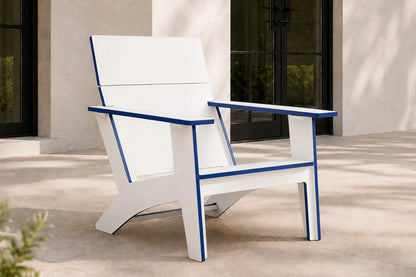 A modern outdoor Adirondack chair with a white frame and blue trim, positioned on a concrete patio in front of a stucco building.