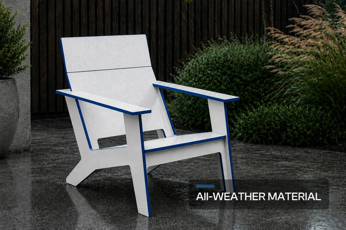 A modern poly Adirondack chair with a white slatted seat and armrests outlined in blue, shown on a wet stone patio with shrubs and a dark fence in the background. A text overlay at the bottom right reads 'All-WEATHER MATERIAL'.