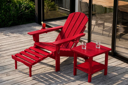 A red outdoor Adirondack chair with an attached footrest and a matching side table on a wooden deck, with glass doors and patio furniture in the background.